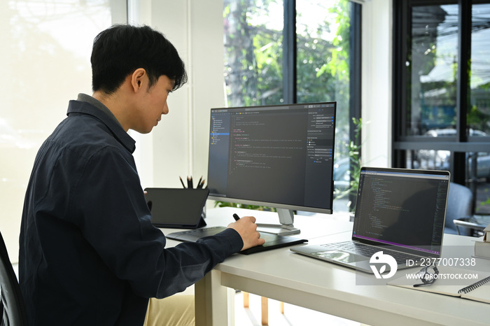 Side view of male programmer sitting front of computers with coded data on screen