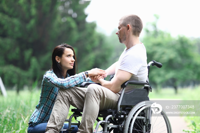 Disabled male veteran is sitting in wheelchair woman is sitting nearby. Difficulties in relationship between man and woman concept