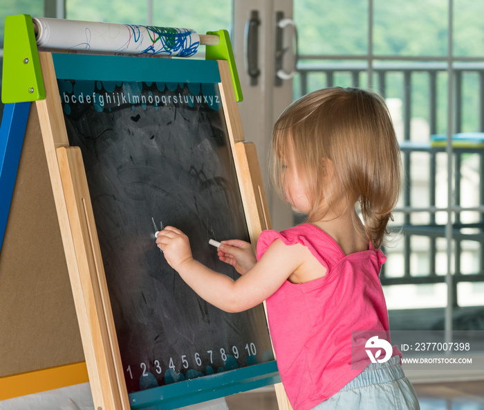 Young baby girl drawing at blackboard