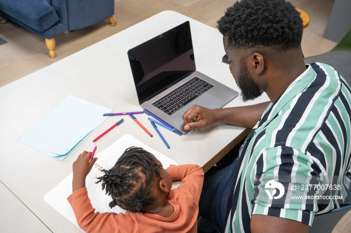 Father using laptop and daughter (2-3) drawing in notepad