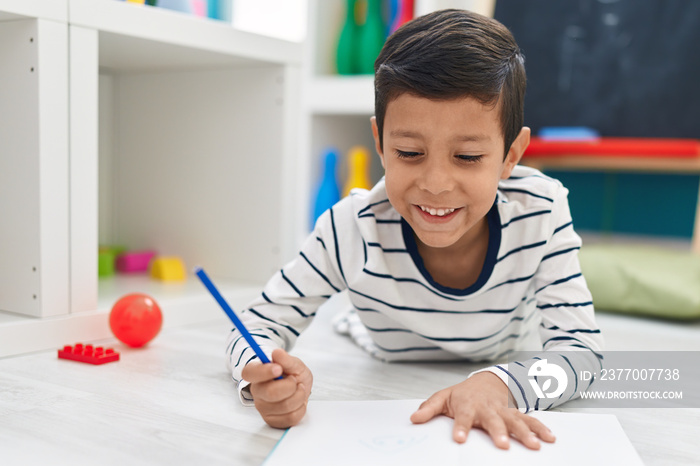 Adorable hispanic boy student writing on notebook at kindergarten