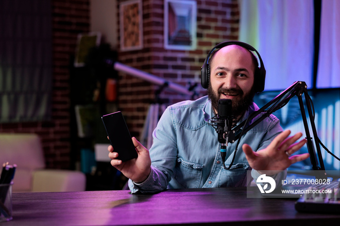 POV of male lifestyle vlogger recommending mobile telephone on podcast, broadcasting live video on social media channel. Cheerful man doing product review with modern smartphone on camera.