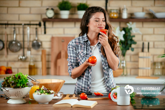 Young woman in kitchen. Beautiful woman smelling tomato.