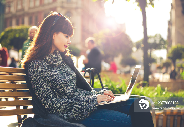 Woman using laptop outdoor sitting in the city street, urban scene