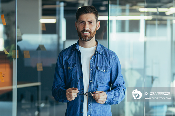 Happy bearded businessman entrepreneur startup owner standing in modern office looking at camera, smiling young hipster, creative man posing in workspace, business portrait