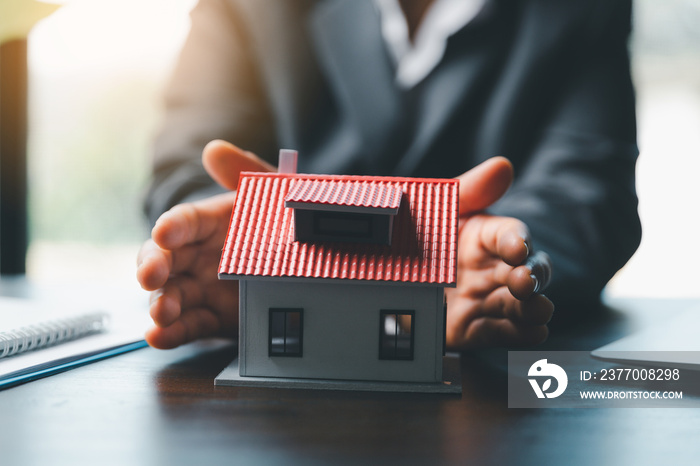 Female hands saving small house with a roof. insurance protective hand over house for protection and care, Concept of home and real estate Property insurance. close up of hands sheltering modern house