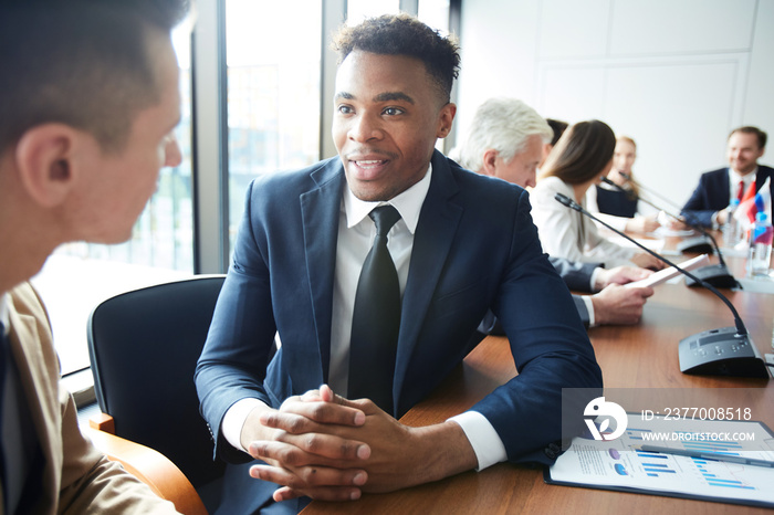 Portrait of African-American businessman talking to colleague while sitting at meeting table in conference room, copy space