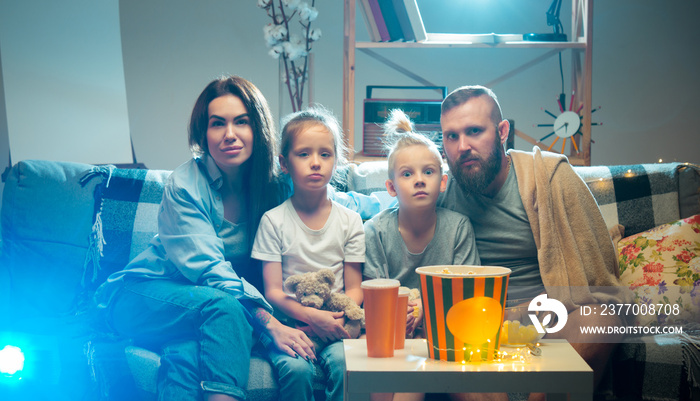 Expressive. Happy family watching projector, TV, movies with popcorn and drinks in the evening at home. Mother, father and kids spending time together. Home comfort, modern technologies, emotions