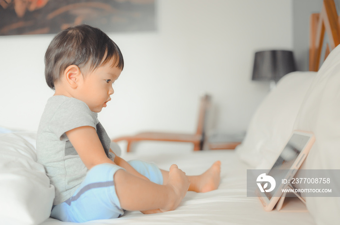 Little asian boy lying in bed and watch a story on touchscreen tablet,Early age education development. Video chat, video call.