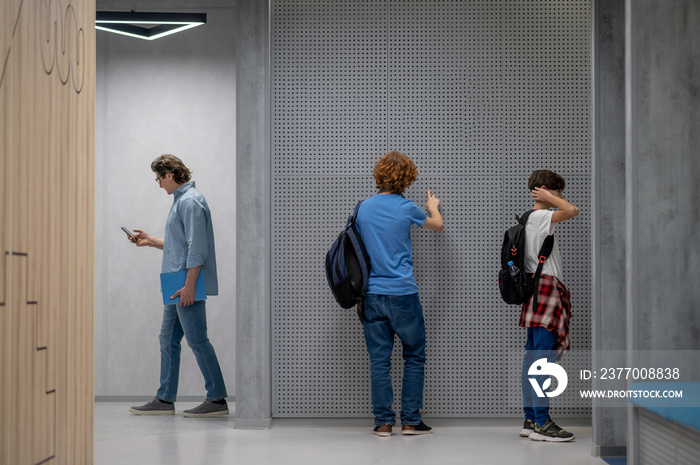 Schoolteacher with the cellphone and pupils in the school lobby