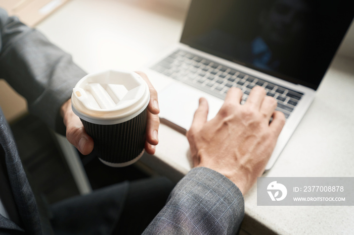 Person holding coffee cup while typing on keyboard