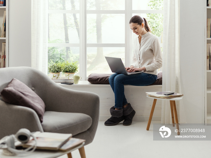 Young woman sitting next to a window and connecting with her laptop