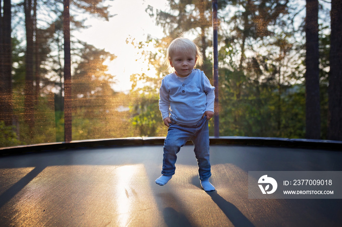 Sweet toddler baby boy jumping on trampoline. Happy little blond child jumping on sunset for the first time