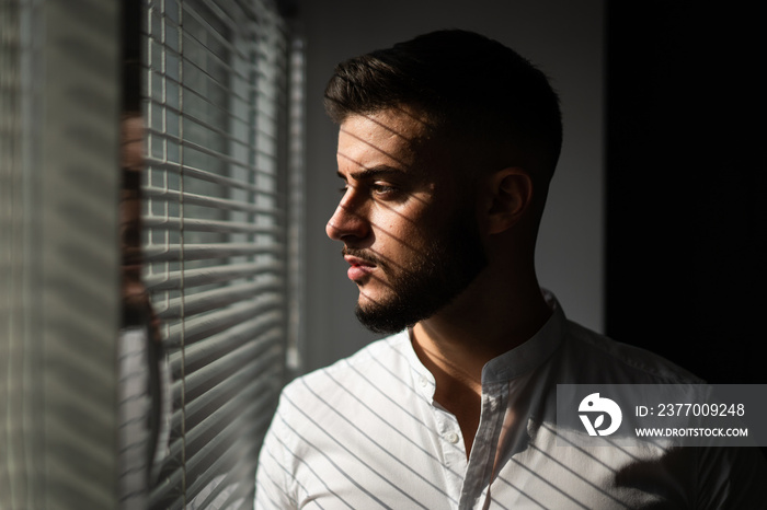 man looking out the window through the blinds to the street, spying. suspected