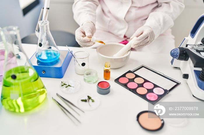 Young hispanic woman wearing scientist uniform pouring liquid on bowl at laboratory