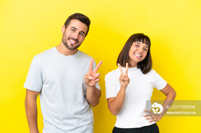 Young couple isolated on yellow background smiling and showing victory sign