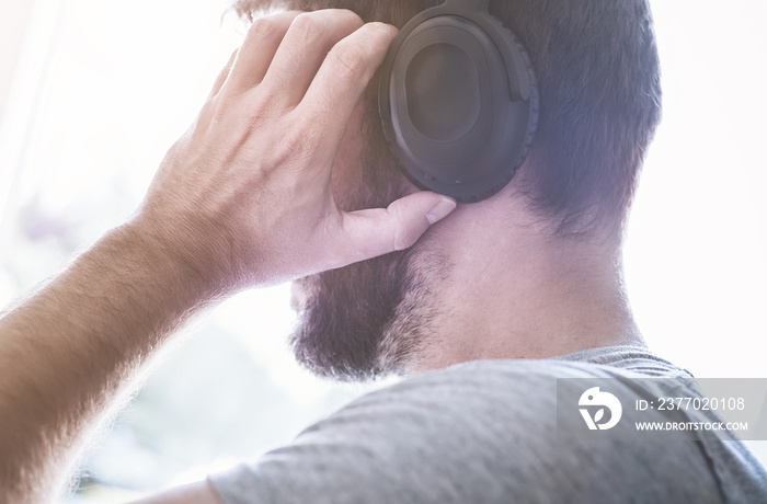 profile view of the head of a young male person listening to music on headphones while adjusting them with his hands