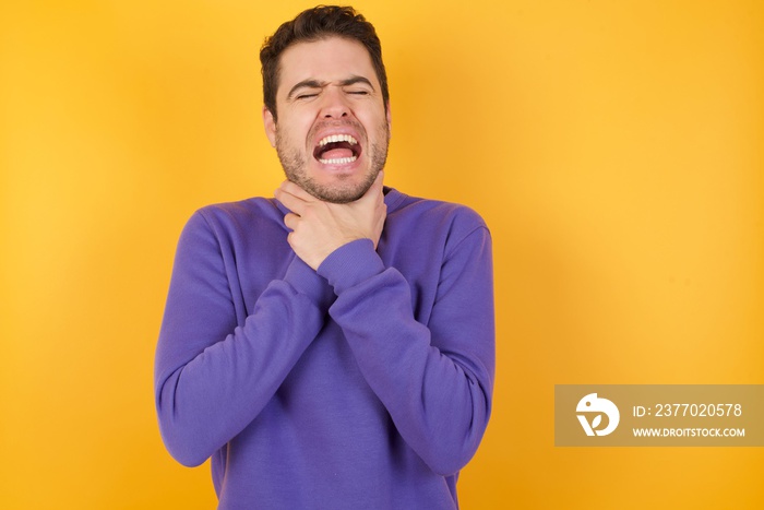 Handsome man with sweatshirt over isolated yellow background shouting suffocate because painful strangle. Health problem. Asphyxiate and suicide concept.