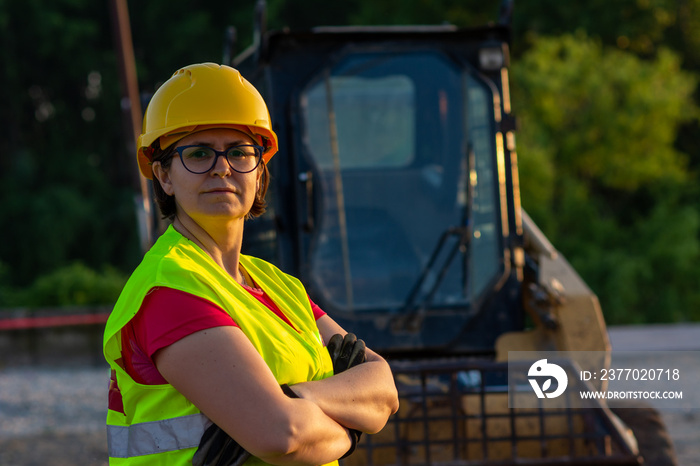 Cheerful female excavator operator on construction site. Woman in reflective clothing operating heavy equipment