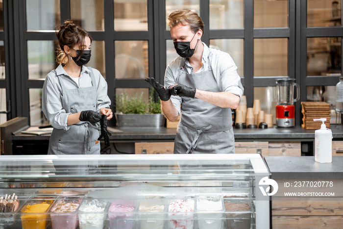 Two sellers in masks and gloves working in the ice cream shop or cafe. Concept of new rules for business during a pandemic