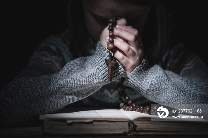 Prayer to God. Close up portrait of young girl pray with rosary and reading the Bible. Horizontal image.