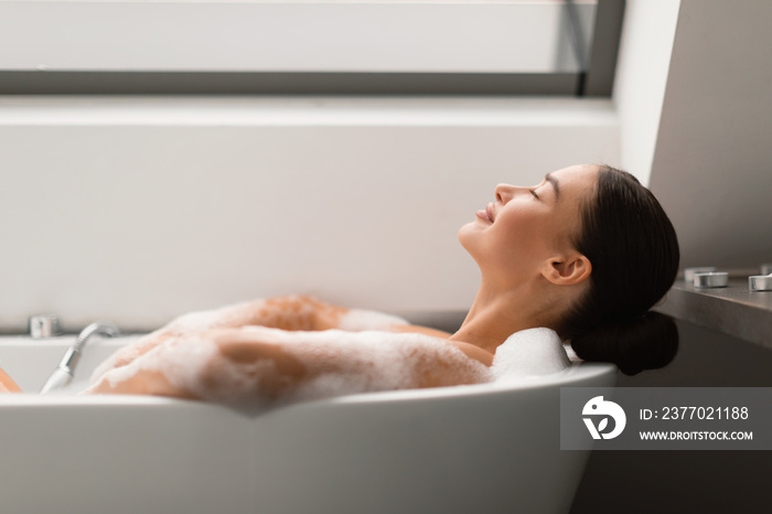 Relaxed Female Taking Bath With Foam Lying In Bathtub Indoors