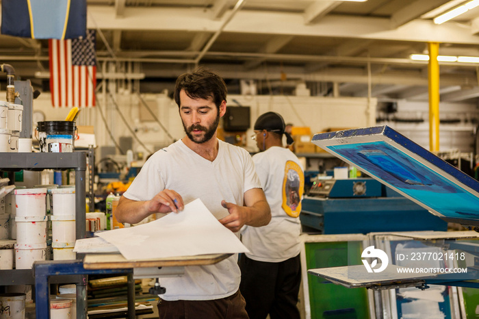 Worker picking up paper in screen print workshop