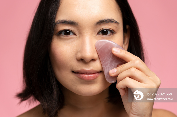 Portrait of smiling beautiful naked asian woman using facial gua sha jade board