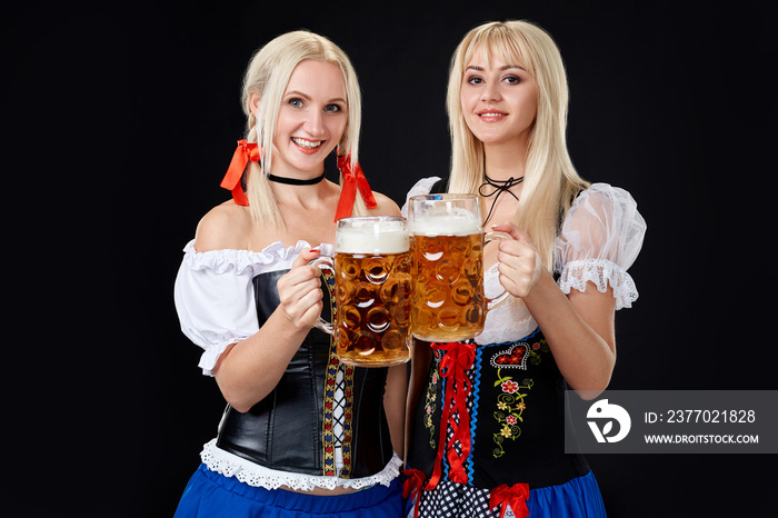 Young and beautiful bavarian girls with two beer mugs on black background