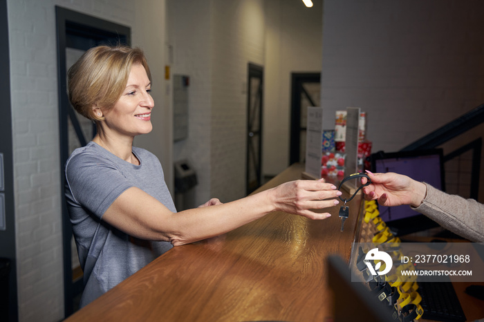 Cheerful woman taking bracelet with key in gym