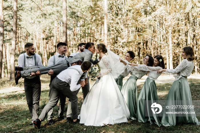 cheerful friends of the groom and bridesmaids holding the newlyweds in their arms, wedding mood, group of friends, funny wedding couple