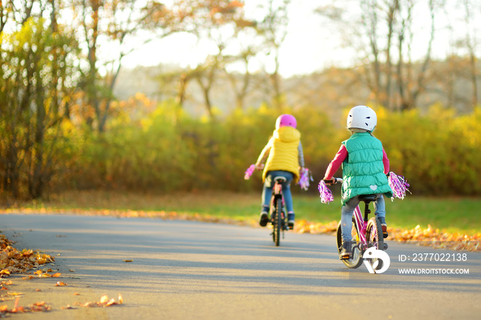 Cute little sisters riding bikes in a city park on sunny autumn day. Active family leisure with kids.