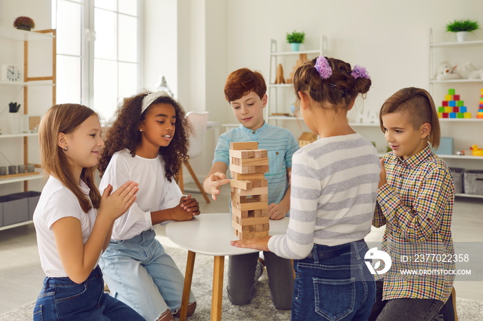 Kids enjoying quiet activities and educational toys. Group of happy diverse 8-10-year-old children playing wood block tower stacking game sitting around table at home or in after school leisure centre