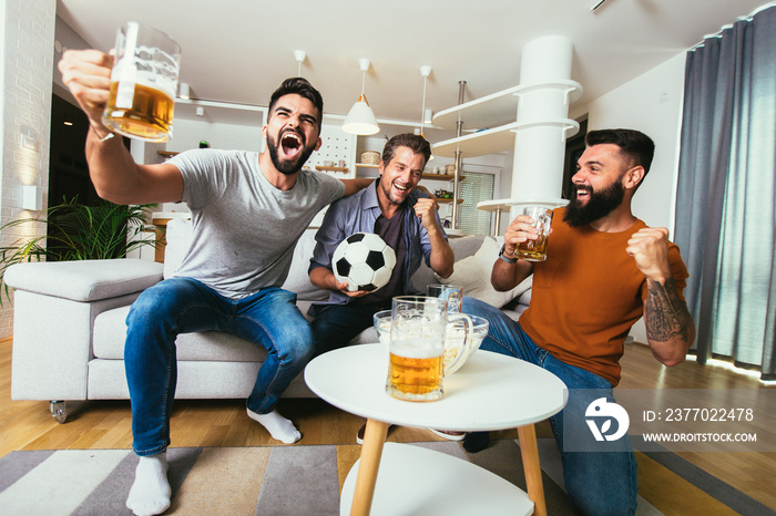 Excited friends watching football game and holding beer and popcorn