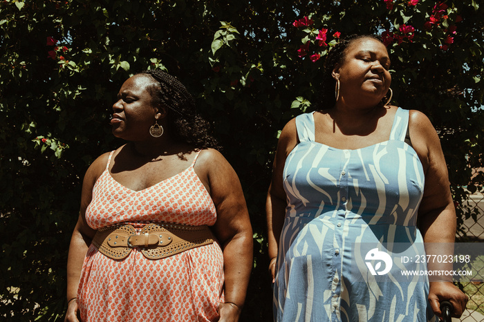 2 African American friends stand outside and have faces in the sun