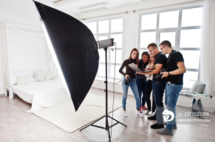 Photographer explaining about the shot to his team in the studio and looking on laptop. Talking to his assistants holding a camera during a photo shoot. Teamwork and brainstorm.