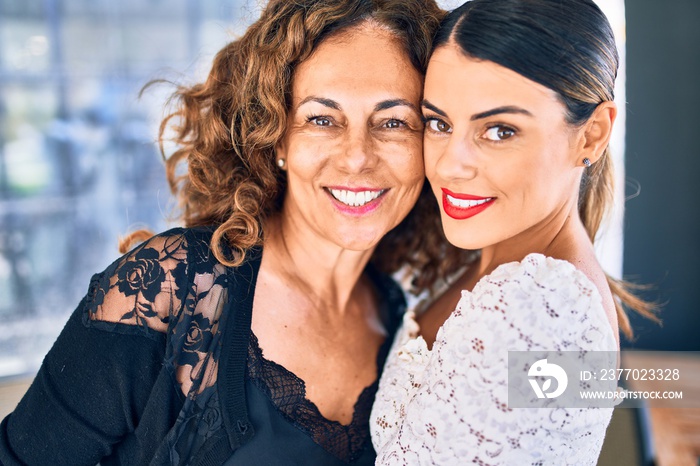 Beautiful mother and daughter smiling happy and confident. Standing with smile on face hugging at restaurant