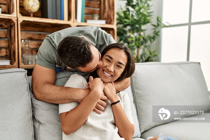 Young latin couple sitting on the sofa hugging at home.