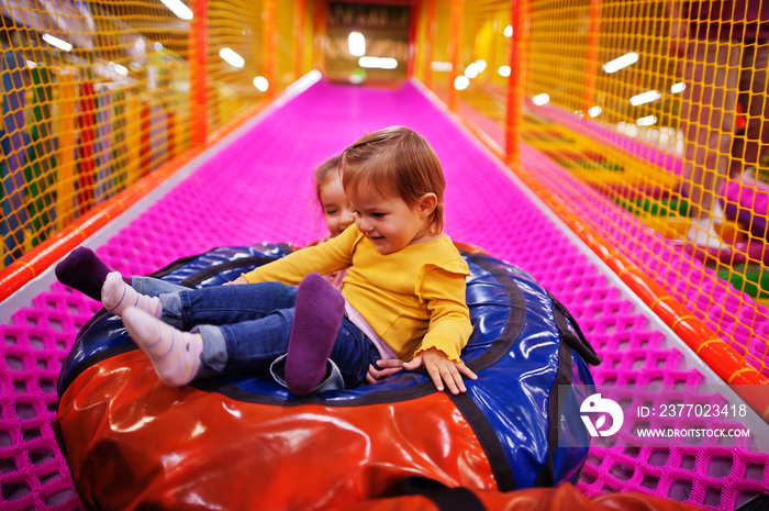 Two sisters sitting in tubing donuts enjoying slides in fun children center.