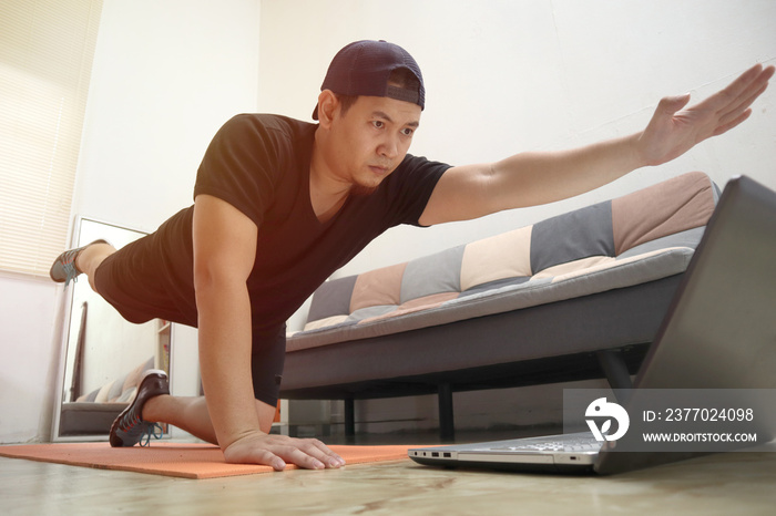 Asian male doing exercise at home while watching online video instruction on laptop, indoor home workout, keep healthy on new normal lifestyle