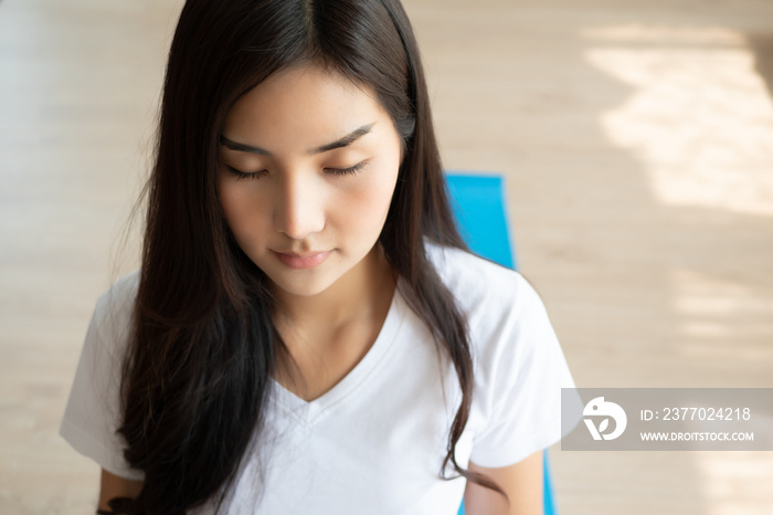 Asian woman doing yoga meditation with relaxed face on yoga mat; Concept of yoga conciousness, body well being, health care, relaxation, hobby, healthy activity; Chinese asian young woman model