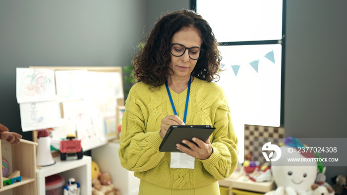 Middle age hispanic woman preschool teacher using touchpad at kindergarten