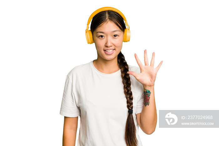 Young asian woman listening to music with headphones isolated smiling cheerful showing number five with fingers.