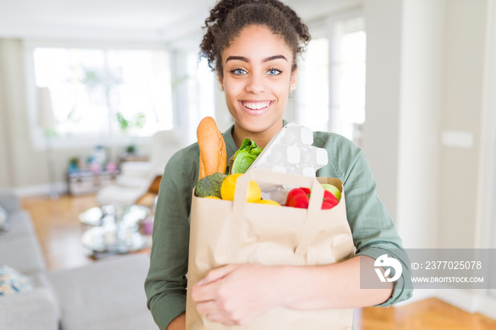 Young african american girl holding paper bag of groceries from supermarket with a happy face standing and smiling with a confident smile showing teeth
