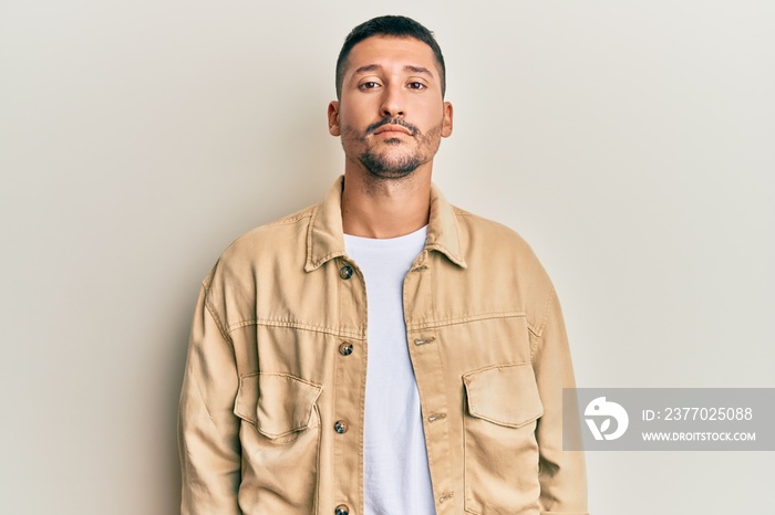 Handsome man with tattoos wearing casual brown denim jacket relaxed with serious expression on face. simple and natural looking at the camera.