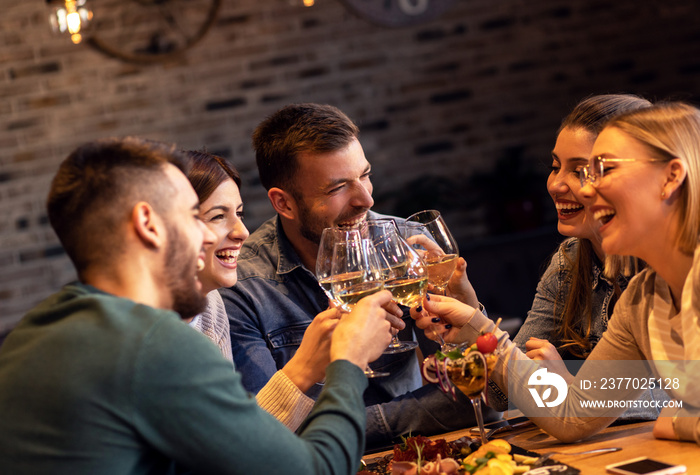 Group of young friends having fun in restaurant, talking and laughing while toasting with glass of wine.