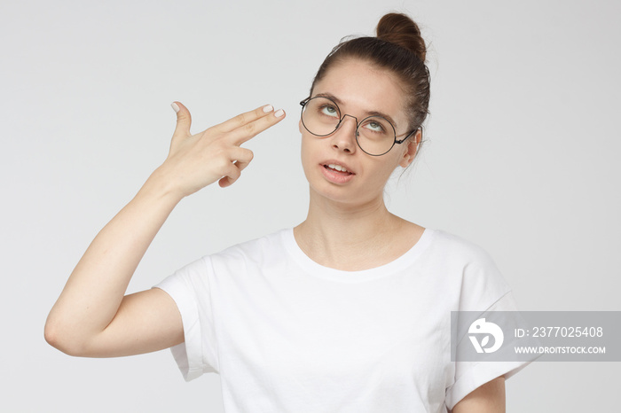 Young woman committing suicide with finger gun gesture, shooting herself making finger pistol sign, isolated on grey background