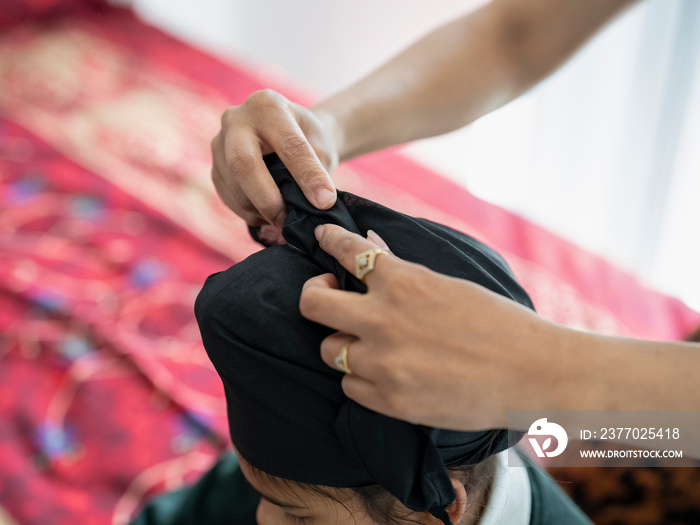 Mother wrapping traditional turban on son’s (6-7) head