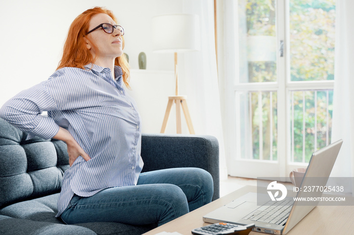 One young redhead woman suffers back pain cramp working at home