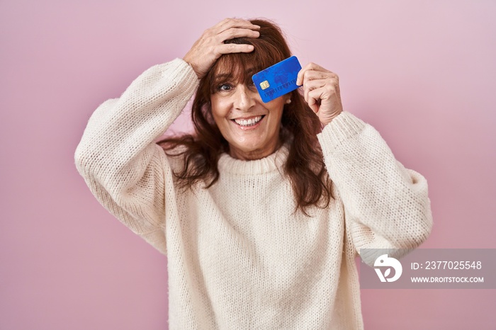 Middle age hispanic woman holding credit card covering eye stressed and frustrated with hand on head, surprised and angry face